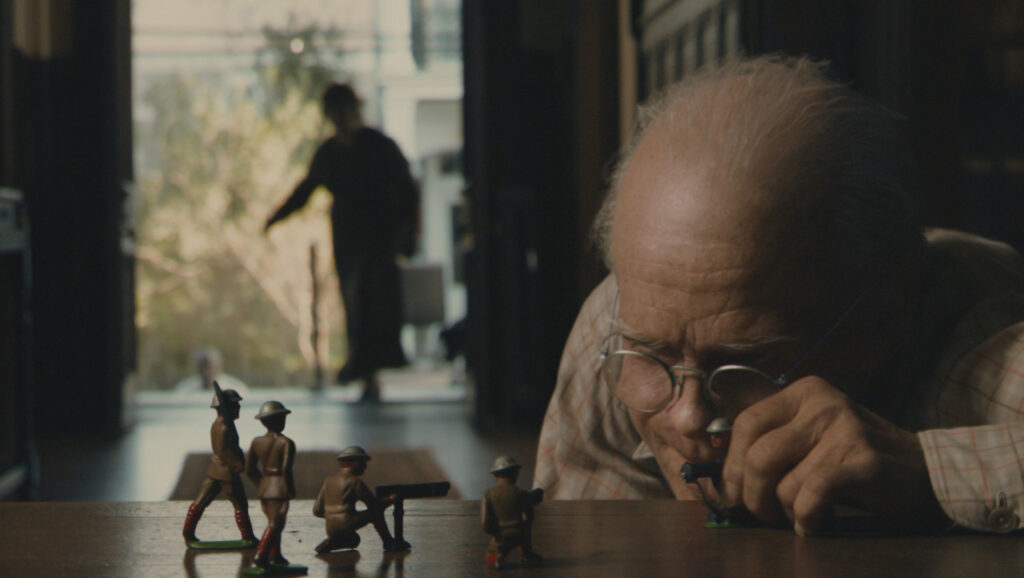 노인의 외모를 한 어린 벤자민이 마룻바닥에 엎드려 장난감 병정 놀이를 하고 있다. 돋보기를 쓰고 장난감에 집중한 그의 모습은 영락없는 아이지만, 주름진 피부와 벗겨진 머리는 80대 노인이다. 문 뒤로 누군가 들어오는 실루엣이 보인다.