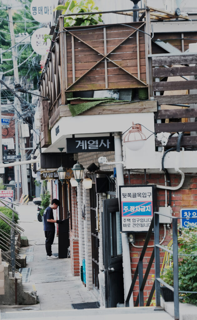 붉은 벽돌 건물과 나무 난간이 어우러진 좁은 골목길에 위치한 부암동 '계열사' 치킨집의 입구 전경