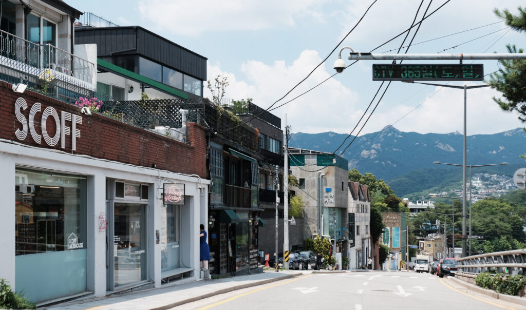하얀 외벽의 스코프(SCOFF) 베이커리 건물과 그 뒤로 웅장하게 펼쳐진 인왕산 능선이 조화를 이루는 부암동 도로 풍경