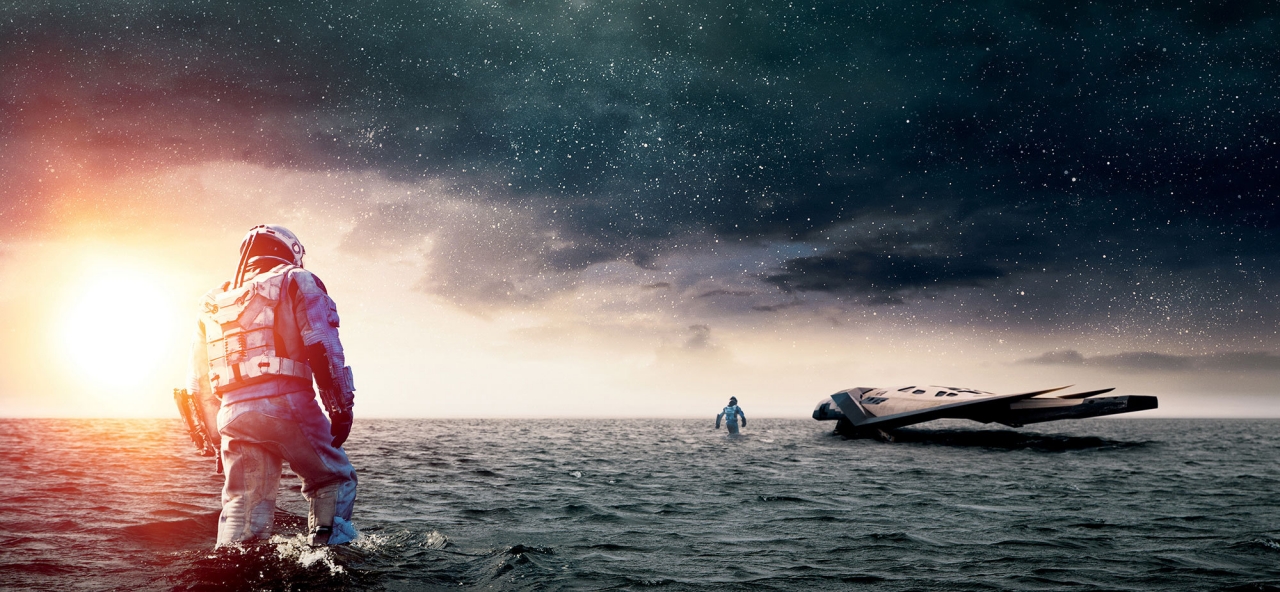 영화 인터스텔라의 밀러 행성 장면. 무릎까지 차오르는 얕은 바다 위에 착륙한 레인저 호와 그 주변을 탐색하는 우주인의 모습. 잿빛 하늘과 끝없는 수평선은 고요해 보이지만, 1시간이 7년으로 흐르는 시간 왜곡과 곧 닥쳐올 거대한 해일의 위협이 공존하는 긴장된 순간을 묘사함.