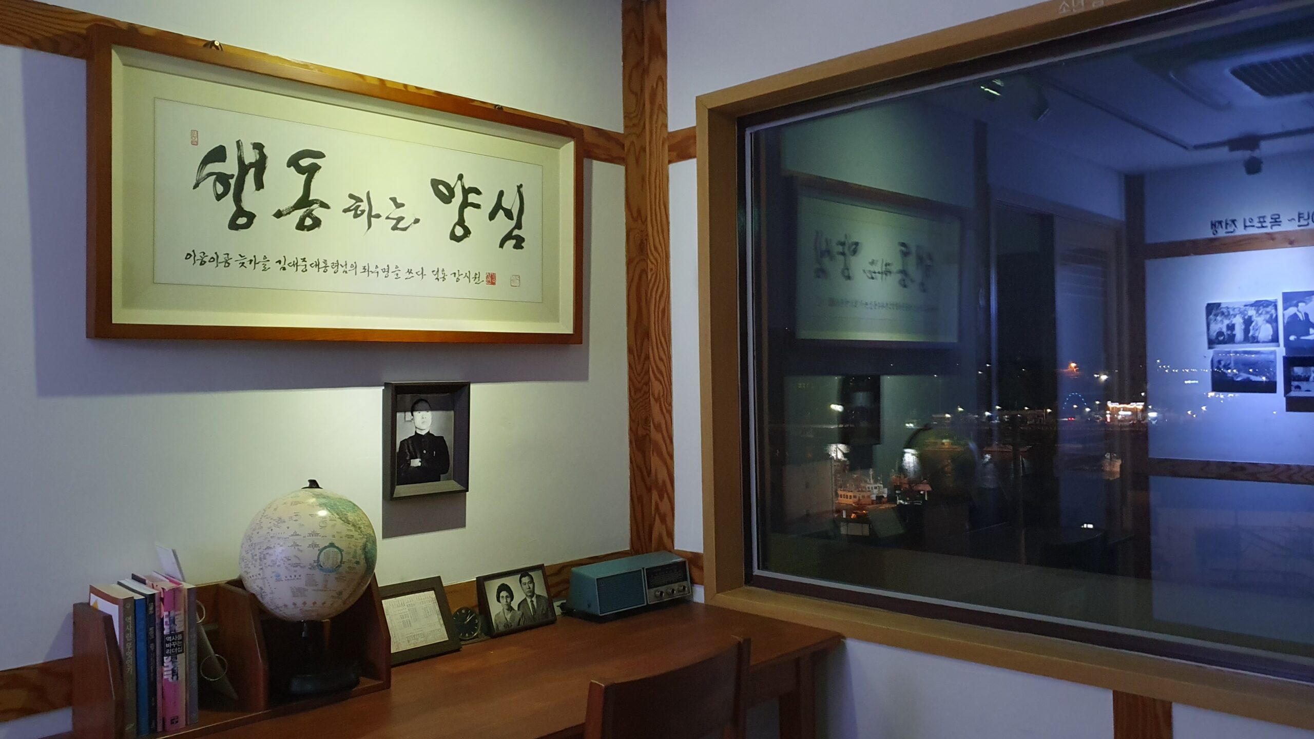 목포 소년 김대중 공부방 내부 모습. 책상 위에는 지구본과 낡은 라디오, 서적들이 놓여 있고, 벽면에는 김대중 전 대통령의 좌우명인 '행동하는 양심' 친필 휘호 액자가 걸려 있다. 창문 너머로 목포의 야경이 비치며, 한국 현대사의 거목이 사색에 잠겼던 공간의 엄숙함을 전한다.