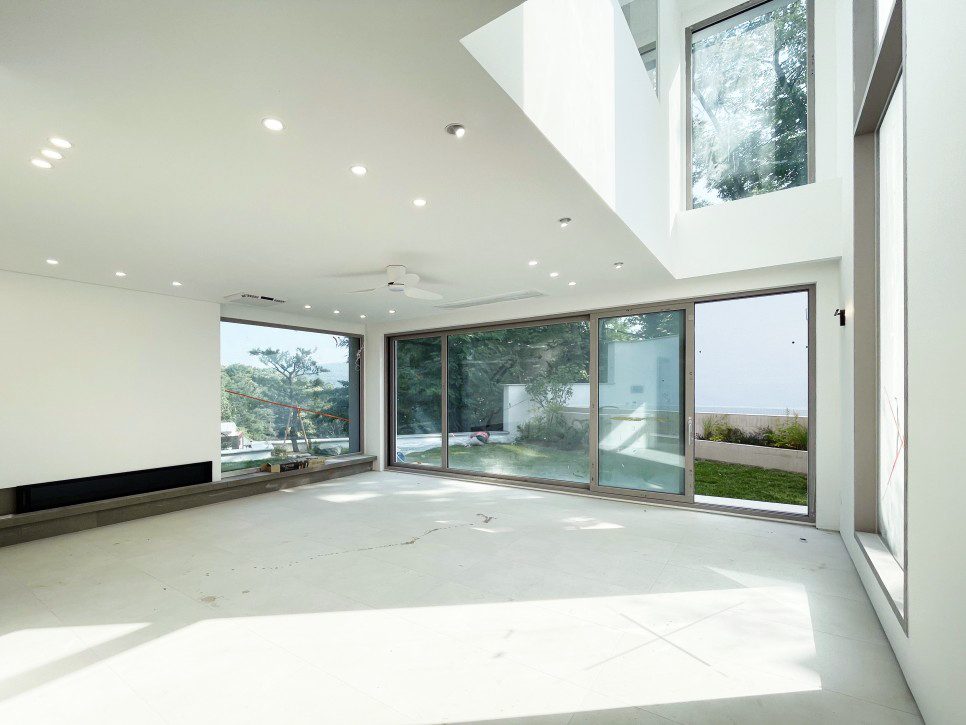 묵화담 거실 인테리어 전경: 여백의 미를 극대화한 높은 층고와 화이트 톤의 미니멀 디자인, 그리고 통창 너머의 자연 조망