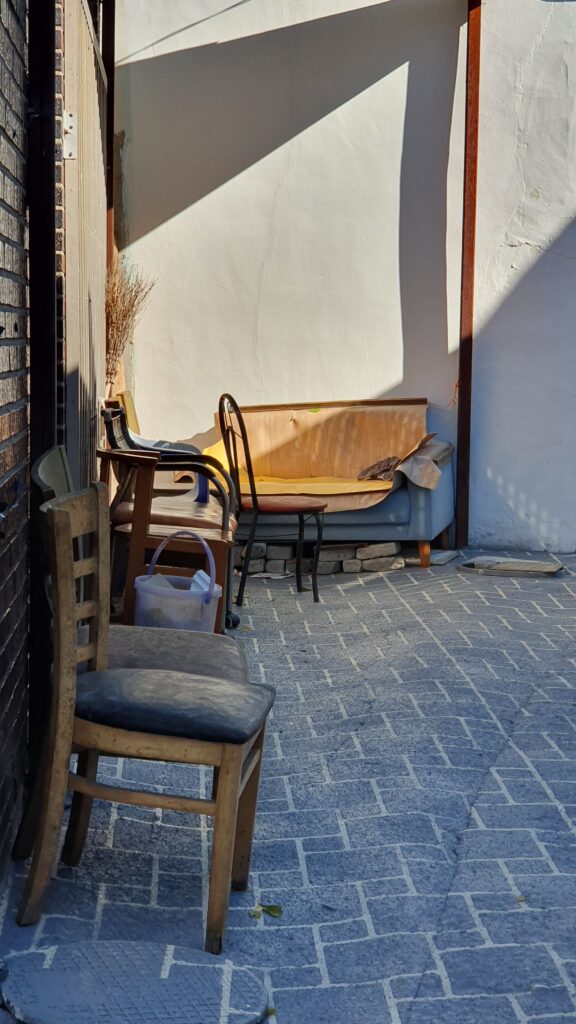 목포 죽교동의 시간이 멈춘 듯한 골목길 풍경. 낡은 담벼락 아래 짝이 맞지 않는 나무 의자와 오래된 소파가 놓여 있고, 그 위로 오후의 따스한 햇살이 쏟아지고 있다. 박화성의 소설 속 주인공들이 살았을 법한 서민들의 소박한 삶의 터전과 골목의 정취를 고스란히 담고 있다.