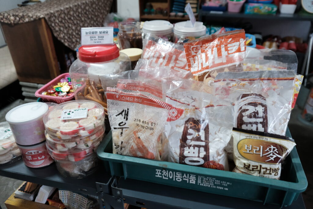 목포 연희네슈퍼 내부에 진열된 1980년대 추억의 간식들. 바나나킥, 새우깡, 보리건빵 등 옛날 포장지의 과자와 추억의 불량식품들이 낡은 선반 위에 놓여 있다. '눈으로만 보세요'라는 문구는 이곳이 실제 상점이 아닌 영화 촬영지로서 보존되고 있음을 보여준다.