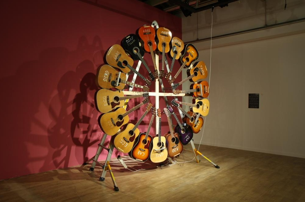 원형 구조물에 여러 대의 낡은 기타가 매달려 스스로 회전하며 연주되는 사운드 설치 작품 전경.