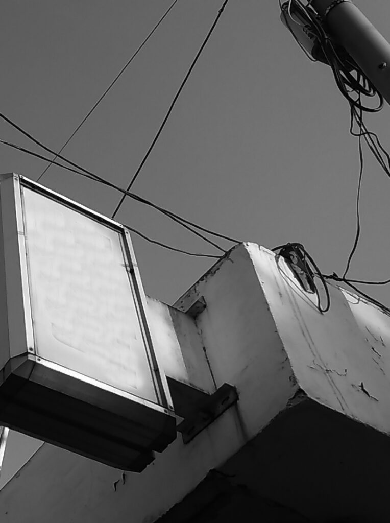 글씨가 모두 지워져 하얗게 바랜 빈 간판과 얽혀있는 전선들이 하늘을 배경으로 보이는 로우 앵글 샷