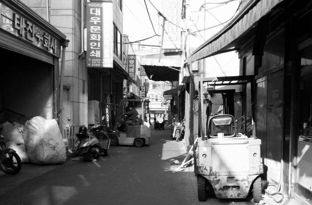 좁은 골목에 지게차와 오토바이가 세워져 있고 '대우문화인쇄' 등 간판이 보이는 흑백 사진