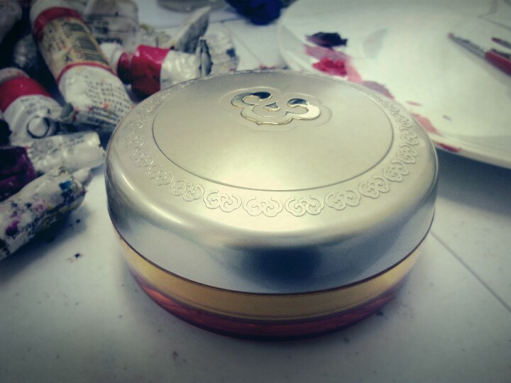 물감 튜브들이 흩어진 작업대 위에 놓인 낡고 둥근 금색 뚜껑의 화장품 분통